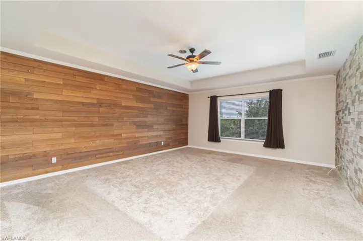 Carpeted spare room featuring ceiling fan, wooden walls, and a raised ceiling