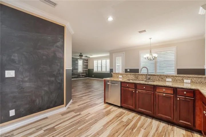 Kitchen with sink, light hardwood / wood-style floors, light stone countertops, ceiling fan with notable chandelier, and dishwasher