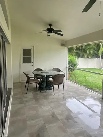 Expansive screened patio featuring large format tile flooring, twin ceiling fans, a white exterior door, and exterior lighting fixtures