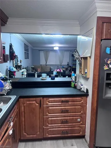 Kitchen featuring stainless steel fridge, ornamental molding, dark countertops, light wood-type flooring, and a textured ceiling