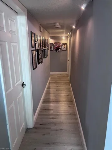 Corridor with a textured ceiling, wood finished floors, and baseboards