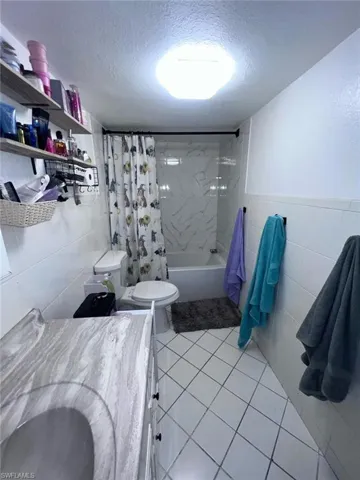 Bathroom featuring tile walls, a textured ceiling, shower / bath combo, toilet, and vanity