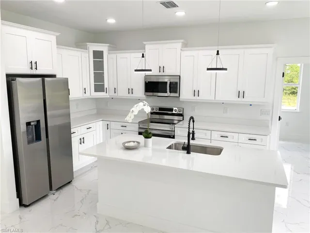 Kitchen featuring sink, hanging light fixtures, white cabinetry, light tile patterned floors, and stainless steel appliances
