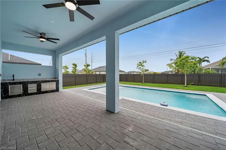 View of pool featuring a ceiling fan, a fenced backyard, a patio area, and an outdoor kitchen