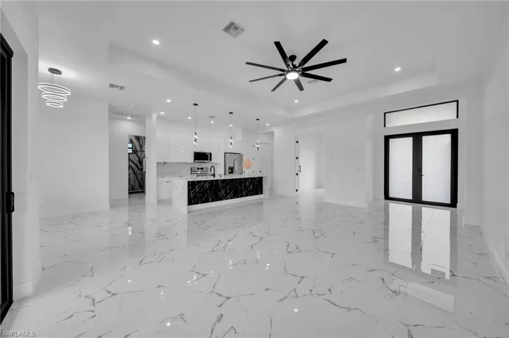 Unfurnished living room with a tray ceiling, recessed lighting, light marble finish floors, a ceiling fan, and french doors