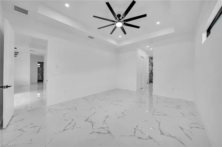 Spare room featuring a raised ceiling, recessed lighting, a ceiling fan, and light marble finish flooring