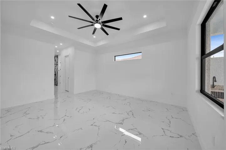 Spare room with a raised ceiling, recessed lighting, light marble finish flooring, and a ceiling fan