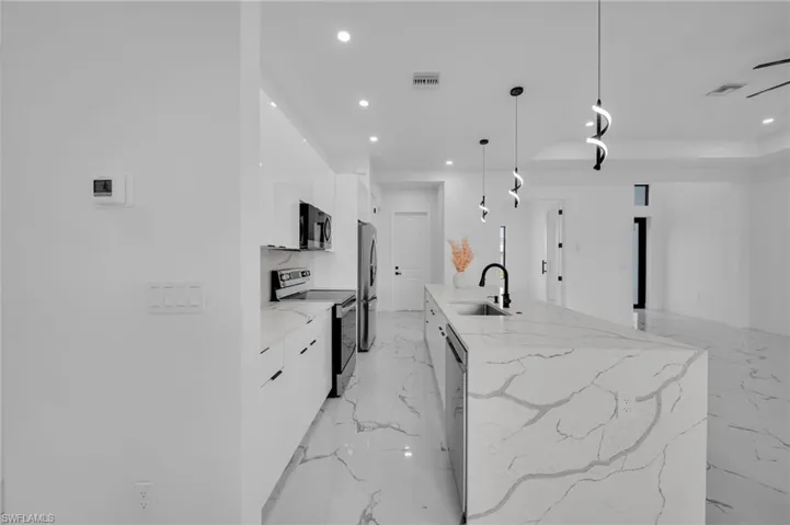 Kitchen featuring modern cabinets, appliances with stainless steel finishes, recessed lighting, white cabinets, and light marble finish flooring