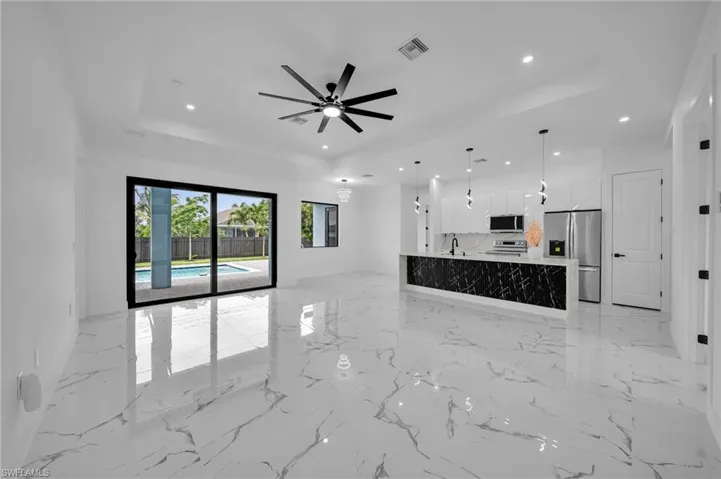 Unfurnished living room featuring a raised ceiling, recessed lighting, light marble finish flooring, and a ceiling fan