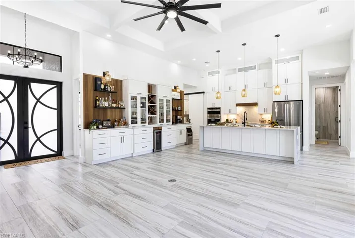 Kitchen and Bar view with chandelier, stainless steel appliances, oversized Quartz island with sink, shaker styled custom cabinetry, and pendant lighting.
