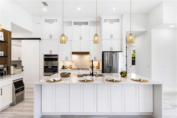 Kitchen featuring stainless steel appliances, a kitchen island with sink, white cabinetry, and Quartz backsplash. Added storage on both sides of the island.