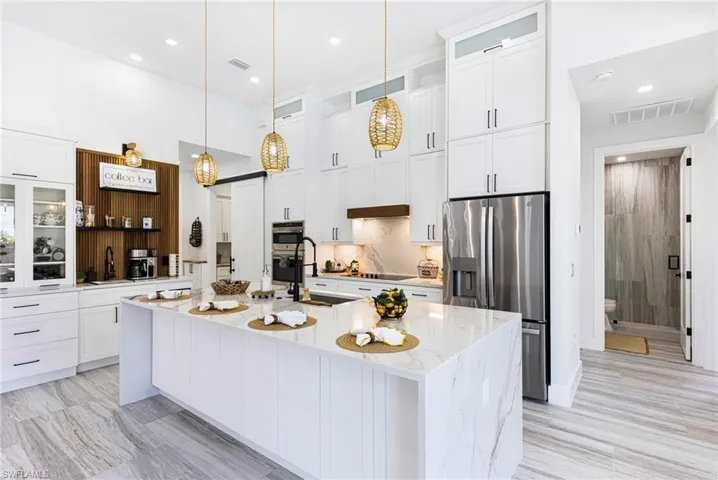 Kitchen featuring an island with sink, light stone counters, pendant light fixtures, recessed lighting, under counter lighting, and Upgraded appliances with stainless steel finishes.