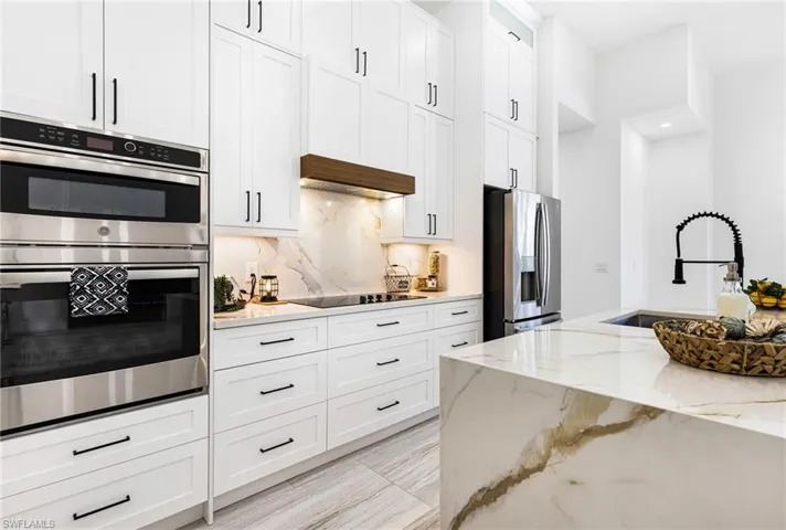 Kitchen featuring white cabinets, custom range hood, stainless steel appliances.