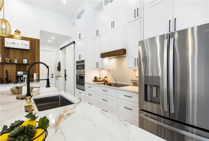 Kitchen featuring custom exhaust hood, stainless steel appliances,Quartz back splash, sink, and white shaker cabinets that reach the ceiling height.
