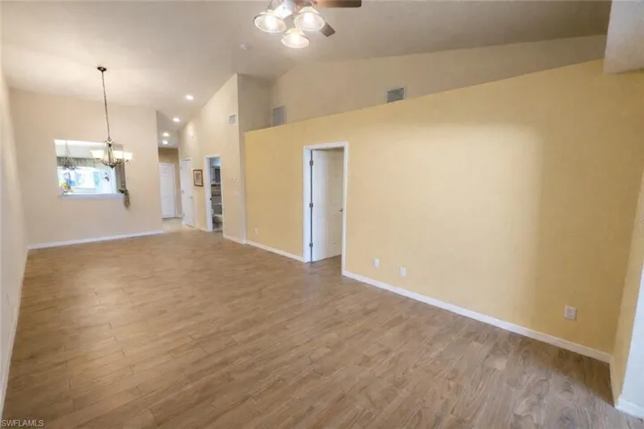 Unfurnished living room featuring light wood-style floors, a chandelier, ceiling fan, recessed lighting, and high vaulted ceiling