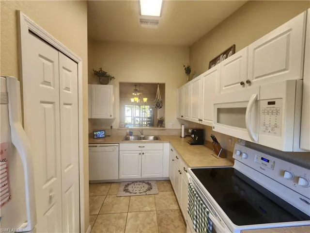 Kitchen featuring white appliances, white cabinets, light countertops, and light tile patterned floors
