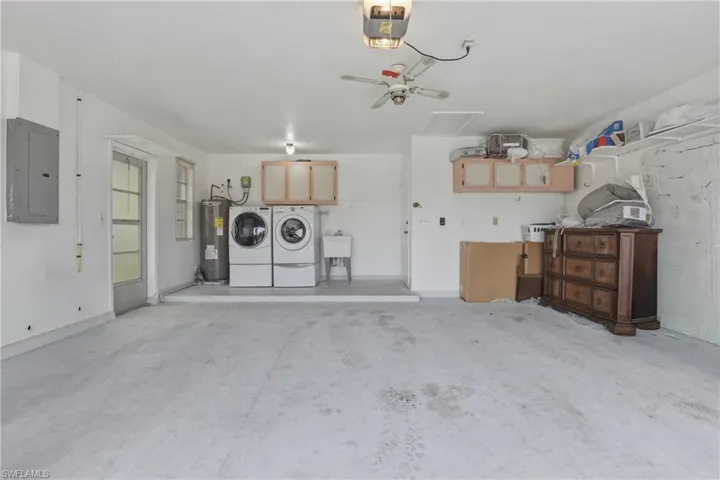 Garage featuring electric panel, a garage door opener, water heater, ceiling fan, and washing machine and clothes dryer