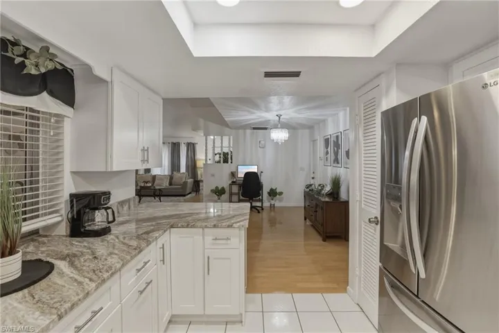 Kitchen featuring stainless steel fridge, white cabinets, light stone countertops, light tile patterned floors, and a chandelier