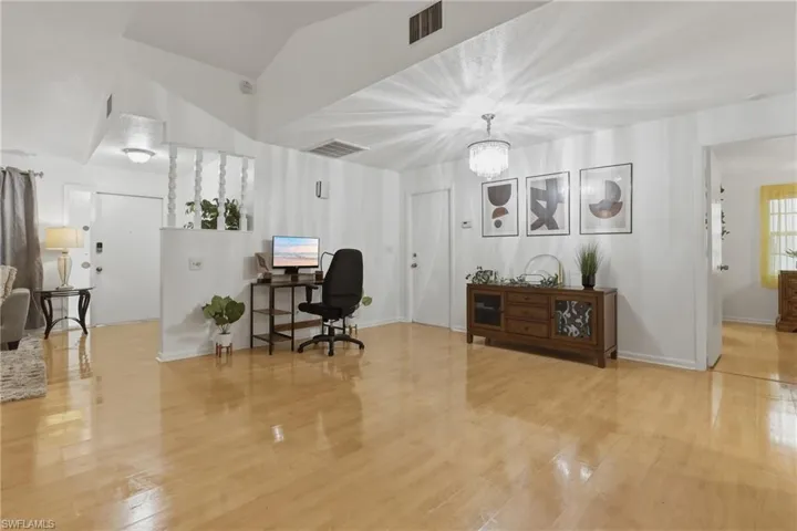 Office space with vaulted ceiling, suspended lighting, and light wood-style floors