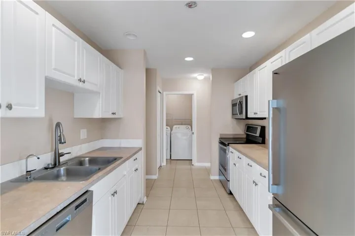 Kitchen featuring stainless steel appliances, sink, light tile patterned floors, white cabinets, and washing machine and dryer