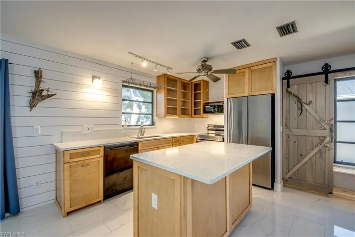 Kitchen with a barn door, black appliances, light brown cabinets, a kitchen island, and wooden walls