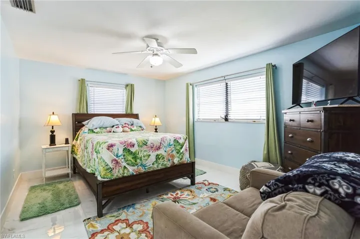 Tiled bedroom with a ceiling fan and multiple windows