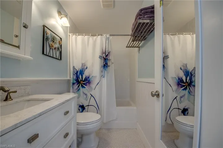 Full bathroom featuring wainscoting, vanity, shower / bathtub combination with curtain, light tile patterned floors, and a decorative wall