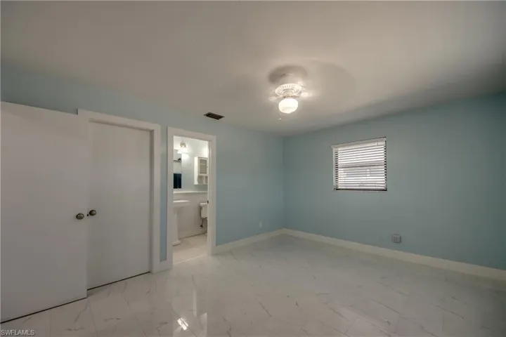 Unfurnished bedroom featuring light marble finish flooring, ceiling fan, and connected bathroom