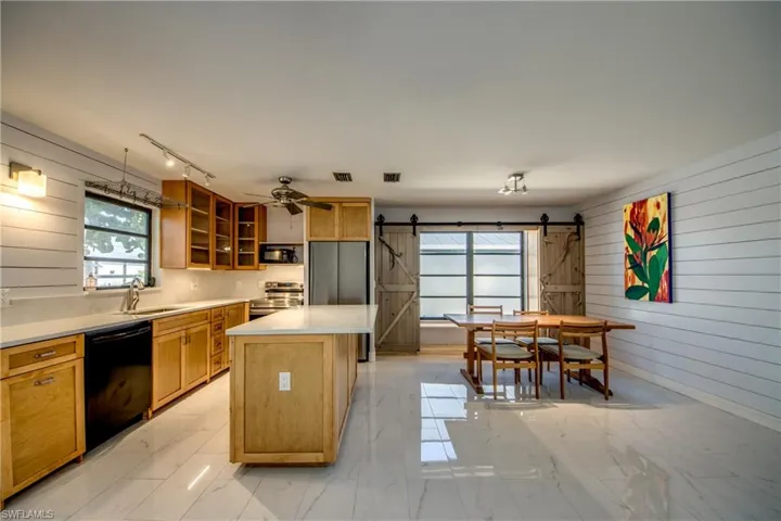Kitchen with wood walls, a barn door, light marble finish flooring, black appliances, and glass insert cabinets