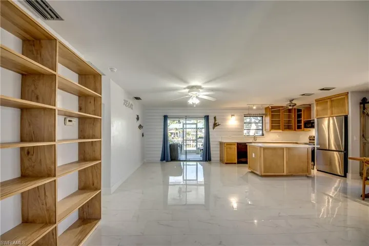Kitchen with glass insert cabinets, light countertops, freestanding refrigerator, light marble finish floors, and a kitchen island