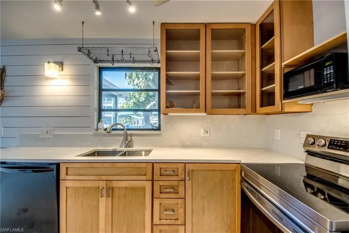 Kitchen with electric range, dishwashing machine, black microwave, light brown cabinetry, and light stone counters
