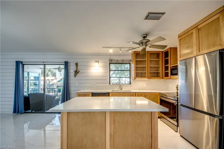 Kitchen featuring black appliances, a kitchen island, wooden walls, ceiling fan, and light marble finish floors