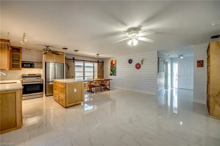 Kitchen featuring a barn door, stainless steel appliances, a ceiling fan, light countertops, and wooden walls
