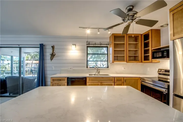 Kitchen featuring black appliances, wooden walls, light stone counters, a ceiling fan, and brown cabinets