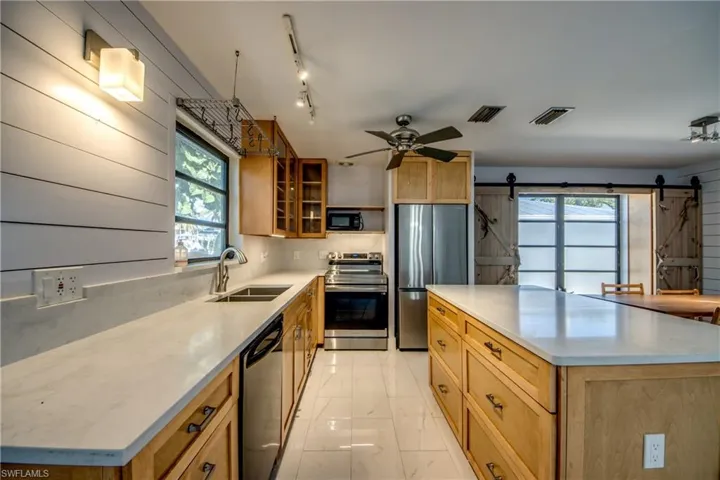 Kitchen with stainless steel appliances, a kitchen island, light marble finish floors, glass insert cabinets, and a barn door