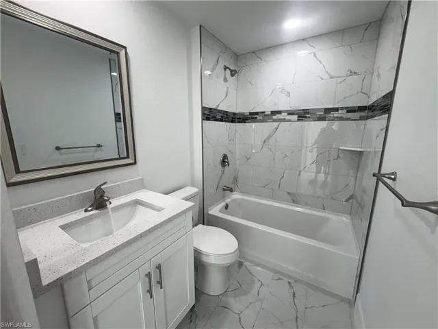 Full bathroom featuring a white vanity with a light speckled countertop, an undermount sink, and a framed mirror