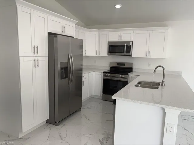 Modern kitchen with white shaker cabinetry, stainless steel appliances, speckled white countertops, and white marbled tile flooring