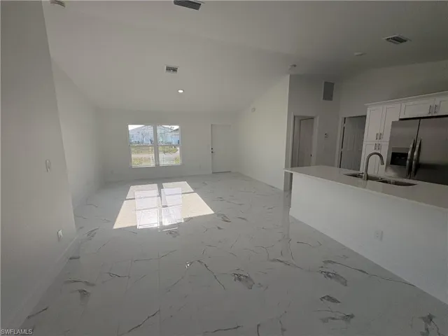 Open-concept living space featuring high vaulted ceilings, large windows, sleek tile flooring, a kitchen island with an undermount sink, and stainless steel appliances