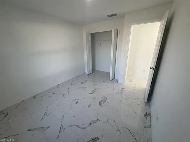 Room featuring large format marble-look tile flooring, white baseboards, and a bi-fold closet with shelving