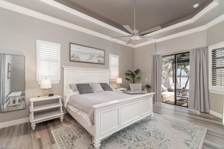Bedroom with access to exterior, a tray ceiling, light wood-style flooring, and baseboards