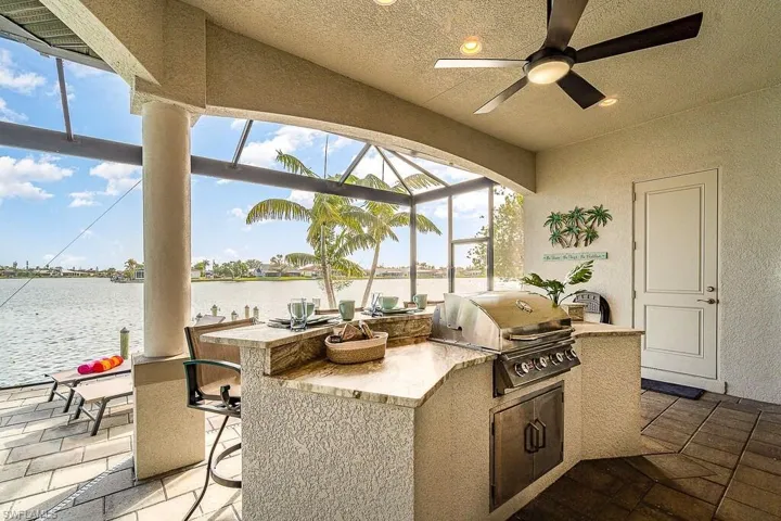 View of patio featuring glass enclosure, outdoor wet bar, area for grilling, a water view, and grilling area