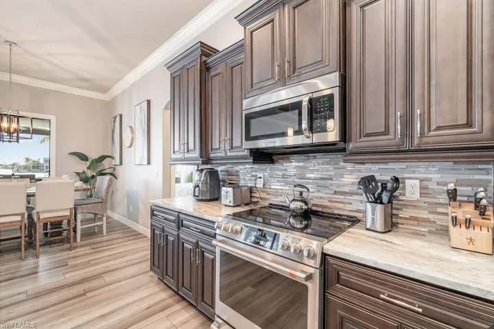 Kitchen with stainless steel appliances, dark brown cabinets, backsplash, decorative light fixtures, and crown molding