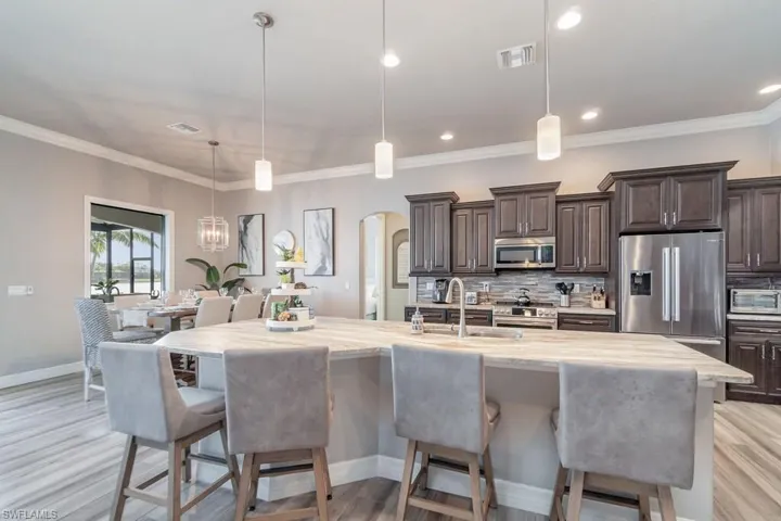 Kitchen with arched walkways, decorative light fixtures, a center island with sink, stainless steel appliances, and a sink