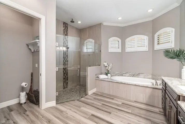 Full bath featuring wood finished floors, a garden tub, crown molding, vanity, and a shower stall