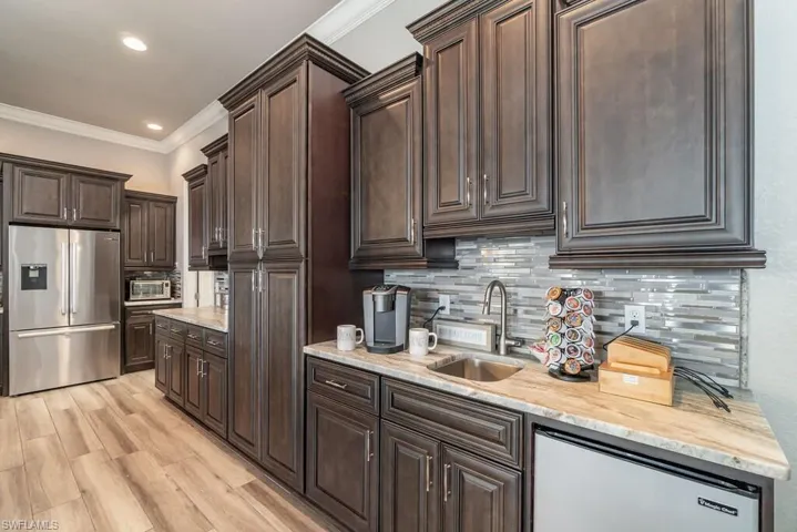 Kitchen featuring dark brown cabinetry, a sink, appliances with stainless steel finishes, tasteful backsplash, and crown molding