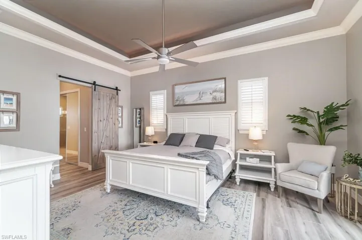 Bedroom featuring light wood-type flooring, a tray ceiling, crown molding, and a barn door