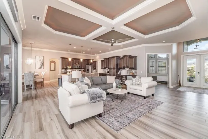 Living area with light wood finished floors, visible vents, coffered ceiling, and french doors