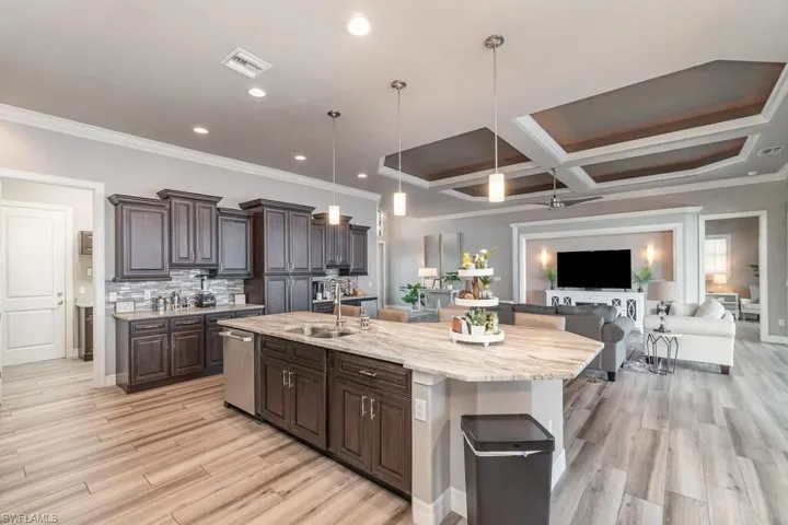 Kitchen featuring dark brown cabinetry, an island with sink, open floor plan, hanging light fixtures, and a sink
