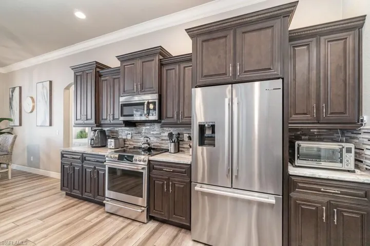 Kitchen with a toaster, light wood-style floors, baseboards, ornamental molding, and appliances with stainless steel finishes