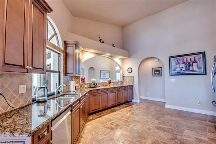 Kitchen with baseboards, stone countertops, arched walkways, a sink, and dishwasher